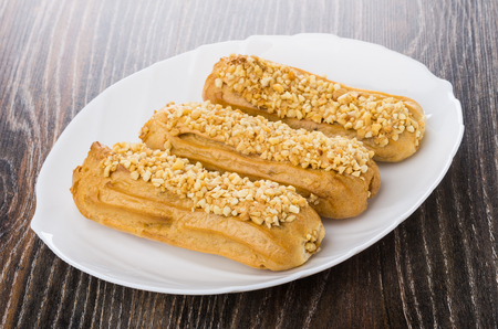 Three eclairs in white dish on wooden table