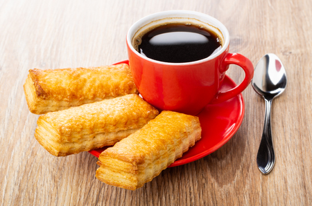 Red cup with coffee, puff cookies on saucer, spoon on wooden tableの写真素材