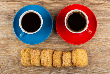 Shortbread cookies, coffee in blue and red cups and saucers on wooden table. Top viewの写真素材