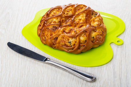 Savory pie with filling on green cutting board, knife on wooden table