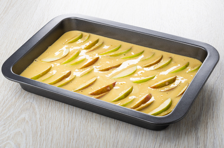 Biscuit dough with slices of apples in baking tray on wooden tableの写真素材