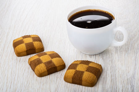 Three checkered shortbread cookies, cup of black coffee on wooden tableの写真素材