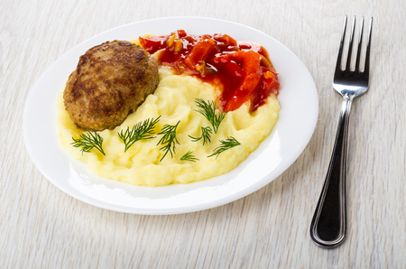 Fried cutlet with mashed potato, lecho in white plate, fork on wooden tableの写真素材