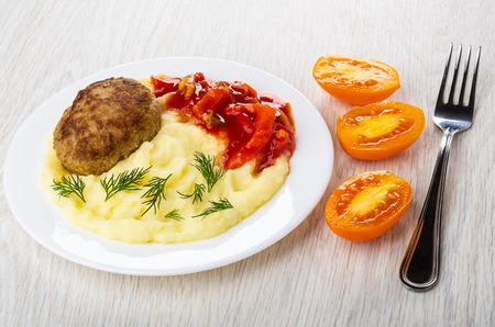 Fried cutlet with mashed potato, lecho in white plate, pieces of tomatoes, fork on wooden table