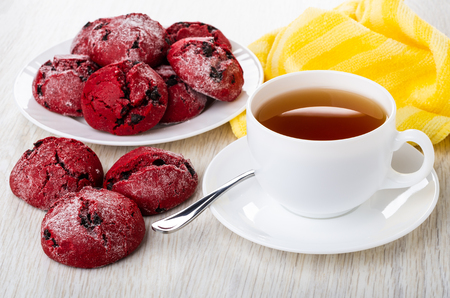 Plate with red shortbread cookies, yellow napkin, cup of tea, teaspoon on saucer on wooden tableの写真素材