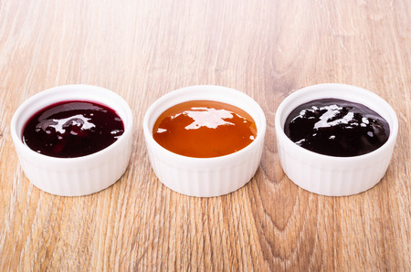 Row of bowls with different jams on wooden table