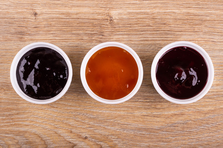 Three bowls with different jams on wooden table. Top view