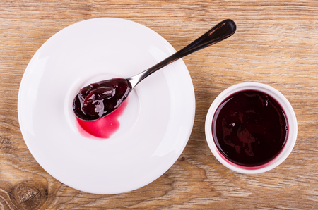 Teaspoon with cherry jam on saucer, bowl with jam on wooden table. Top viewの写真素材
