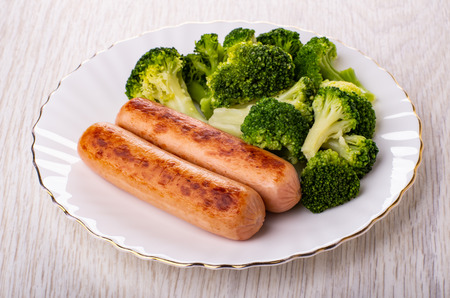 Boiled broccoli with fried sausages in plate on wooden tableの写真素材