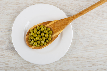 Canned green peas in bamboo spoon in white plate on light wooden table. Top viewの写真素材