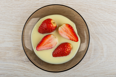 Halves of strawberry in condensed milk on brown saucer on wooden table. Top viewの写真素材