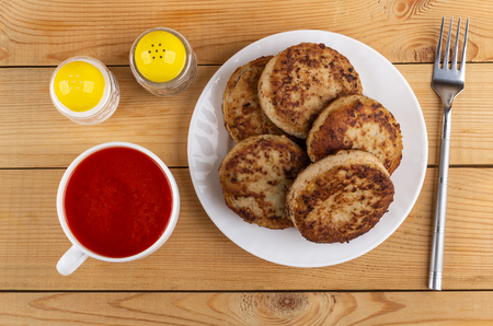 Plate with fried cutlets, cup with tomato juice, salt and pepper shakers, fork on wooden table. Top viewの写真素材