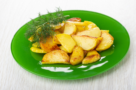 Fried potatoes and dill in green plate on wooden tableの写真素材