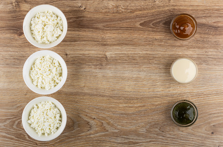 Row of bowls with cottage cheese, row of bowls with boiled condensed milk, condensed milk, gooseberry jam, and spoons on wooden table. Top viewの写真素材