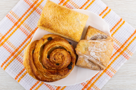 Different sweet pastry in white dish on checkered napkin on wooden table. Top viewの写真素材