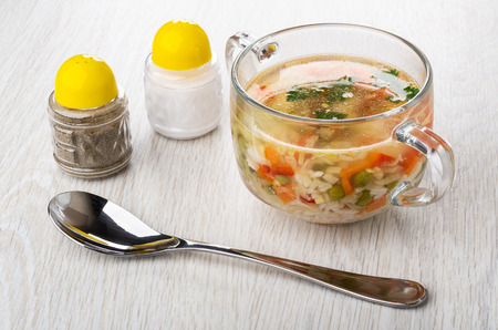 Soup with chicken meat, rice and vegetables in glass transparent bowl, salt and pepper shakers, spoon on wooden tableの写真素材