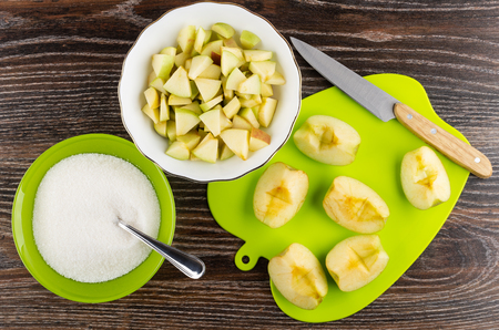 Pieces of apples, kitchen knife on cutting board, bowl with chopped apples, spoon in green bowl with sugar on wooden table. Top viewの写真素材