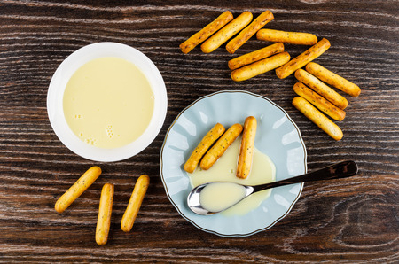 Bread sticks with poppy, bowl with sweet condensed milk, teaspoon and breadsticks with milk on blue saucer on wooden table. Top viewの写真素材