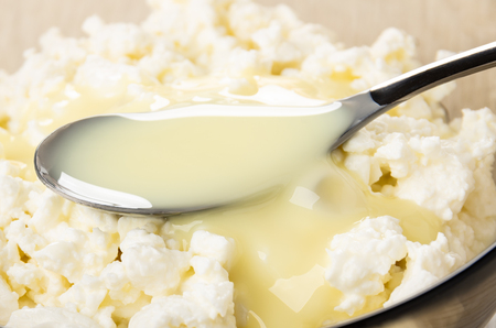 Close up of teaspoon with sweet condensed milk in bowl with cottage cheeseの写真素材