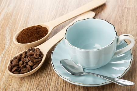 Wooden spoons with roasted coffee beans and ground coffee, empty blue cup, spoon on saucer on wooden tableの写真素材