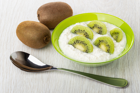 Unpeeled kiwi, bowl with cottage cheese and slices of kiwi fruits, spoon on wooden tableの写真素材