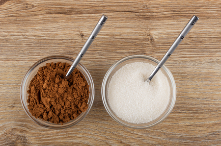 Cacao powder, teaspoon in bowl, teaspoon in bowl with sugar on wooden table. Top viewの写真素材