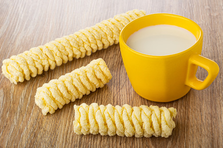 Pieces of cornflakes pigtails, yellow cup with milk on wooden tableの写真素材