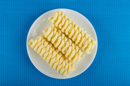 Three pieces of cornflakes pigtails in white saucer on blue table. Top viewの写真素材