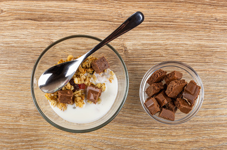 Teaspoon in transparent bowl with granola, yogurt, chocolate, bowl with pieces of porous chocolate on wooden table. Top viewの写真素材