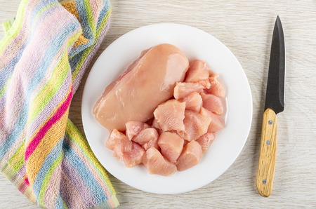 Striped napkin, white glass plate with pieces of raw chicken breast, kitchen knife on wooden table. Top viewの写真素材