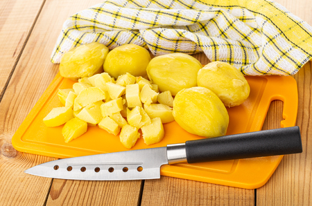 Checkered napkin, pieces of baked potatoes, kitchen knife on orange cutting board on wooden tableの写真素材