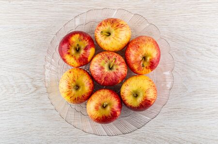 Red fresh stripe apples in transparent glass dish on wooden table. Top viewの写真素材