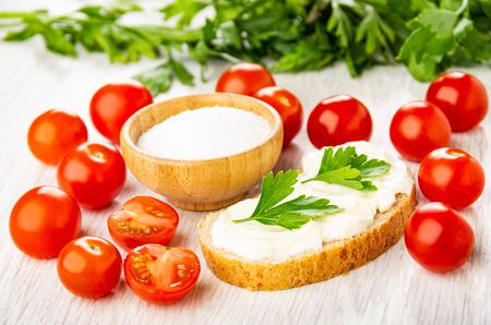 Fresh red tomato cherry, bamboo bowl with sea salt, sandwich with melted cheese, parsley on wooden tableの写真素材