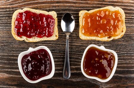 Sandwiches with currant jam, apricot jam, teaspoon, bowls with jam on dark wooden table. Top viewの写真素材