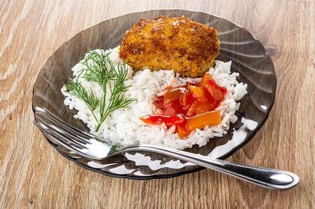 Fork in transparent brown plate with fried patty, rice, lecho, dill on wooden tableの写真素材