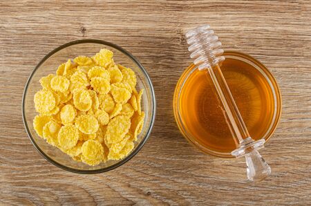 Transparent bowl with corn flakes, honey dipper on bowl with liquid honey on wooden table. Top view