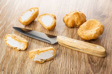 Halves of profiteroles, whole profiteroles, kitchen knife on wooden table