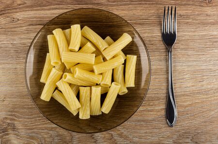 Brown transparent plate with cooked pasta, fork on wooden table. Top viewの写真素材
