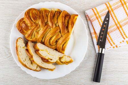 Wicker pie with lemon jam, slices of pie in white glass dish, kitchen knife on checkered napkin on wooden table. Top viewの写真素材