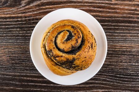 Sweet bun with poppy in white saucer on dark wooden table. Top viewの写真素材