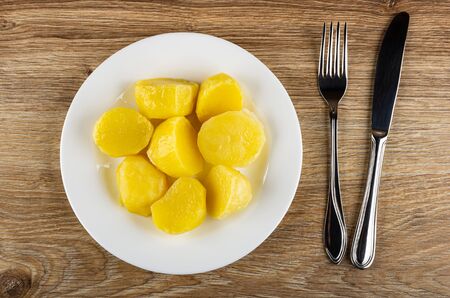 Pieces of baked potato in white glass plate, fork and table knife on wooden table. Top viewの写真素材