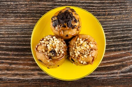 Three cakes with chocolate and peanuts in yellow saucer on dark wooden table. Top viewの写真素材