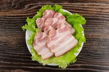 Slices of smoked pork brisket on leaves of lettuce in white plate on dark wooden table. Top viewの写真素材