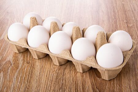 Cardboard container with raw chicken eggs on wooden table