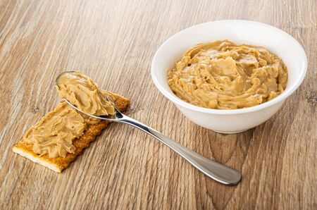 Sandwich from cracker with peanut butter, teaspoon, bowl with peanut butter on wooden table