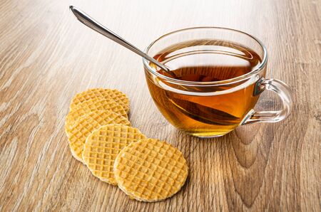 Few wafers, teaspoon in transparent cup with tea on wooden tableの写真素材