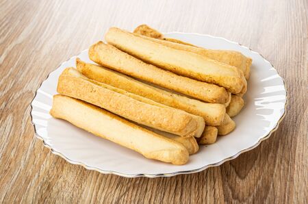 Salted bread sticks in glass plate on brown wooden table