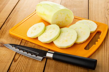 Pieces of peeled marrow squash, slices of squash, kitchen knife on cutting board on wooden tableの写真素材
