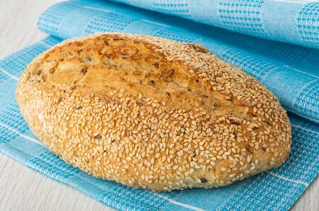 Loaf of fresh baked bread with sesame  on blue napkin on wooden table