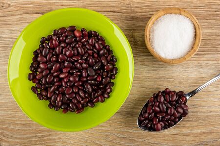 Raw red bean in glass green bowl, salt in bowl, beans in metallic spoon on wooden table. Top viewの写真素材